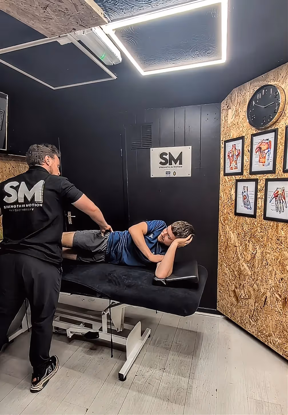 Physiotherapist in a black shirt stretching the leg of a patient lying on a treatment table in a therapy room.