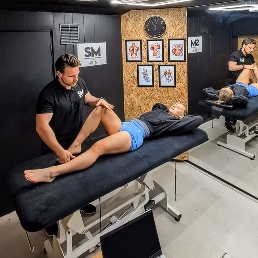 Physical therapist stretches the leg of a woman lying on a treatment table in a therapy room.